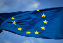 En blå EU-flagga med tolv gula stjärnor vajande mot en blå himmel.