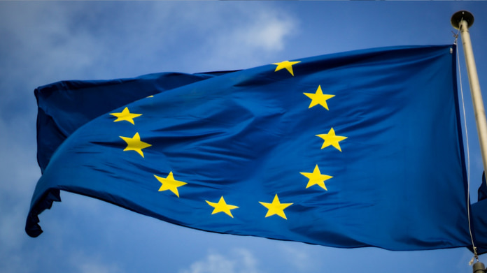 En blå EU-flagga med tolv gula stjärnor vajande mot en blå himmel.