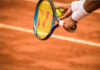 En tennisspelare förbereder sig för att serva på en grusbana med racket och boll i handen.